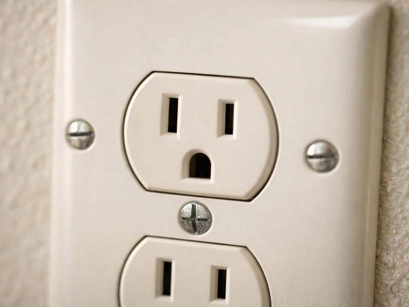 Close-up of a beige wall outlet with two sockets and visible metal screws on a textured wall
