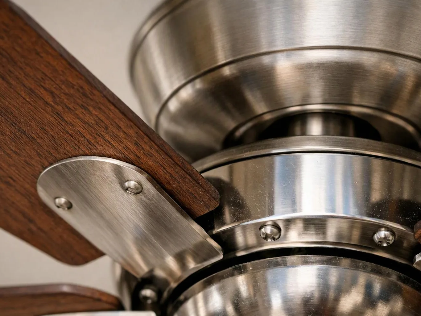 Close-up of a ceiling fan hub with brushed metal parts and dark wooden blades against a plain background