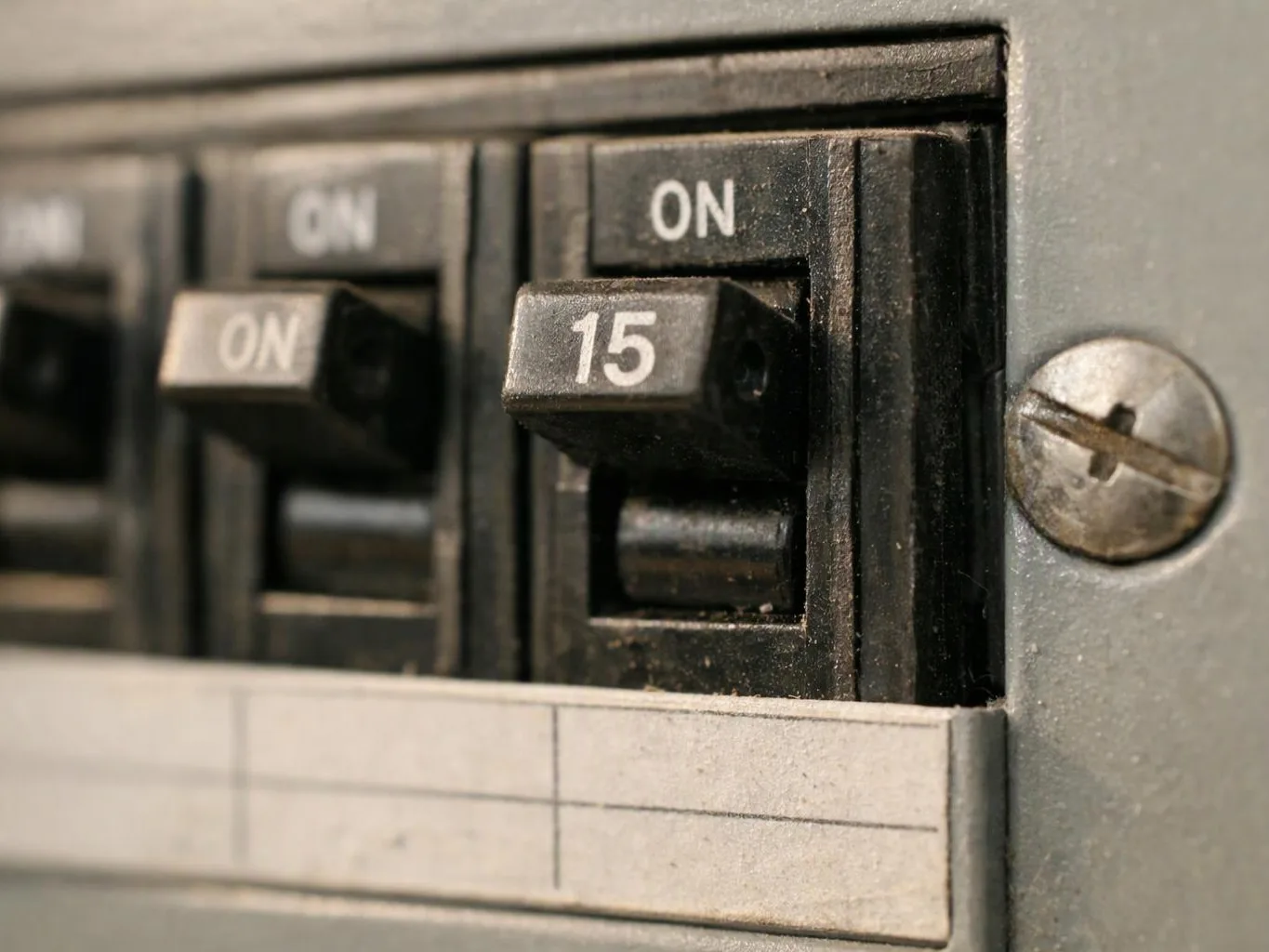 Close-up of a circuit breaker panel with black switches marked on and 15 next to a silver screw