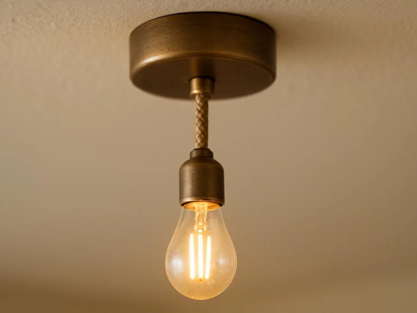A glowing light bulb hangs from a brass ceiling fixture against a plain beige ceiling